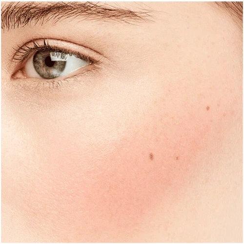 Close-up of cheek with natural pink liquid blush makeup applied, showing smooth skin texture.