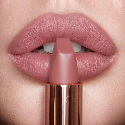 Close-up of lips with matte pink nude lipstick, lipstick held near mouth